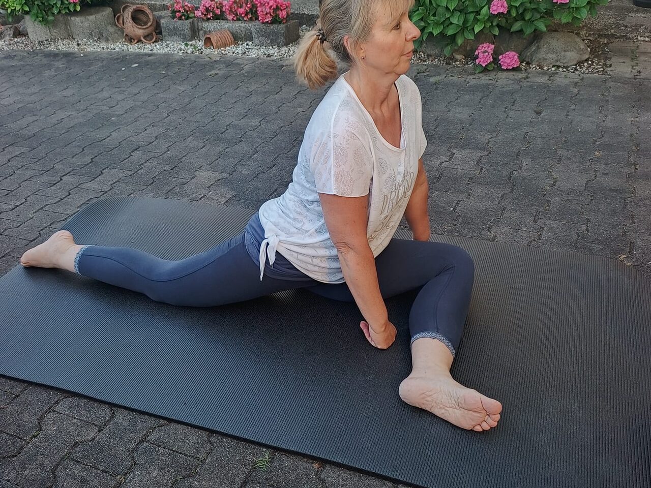 Melanie sitzt aufgerichtet in einer ruhigen Dehnhaltung auf der Matte.